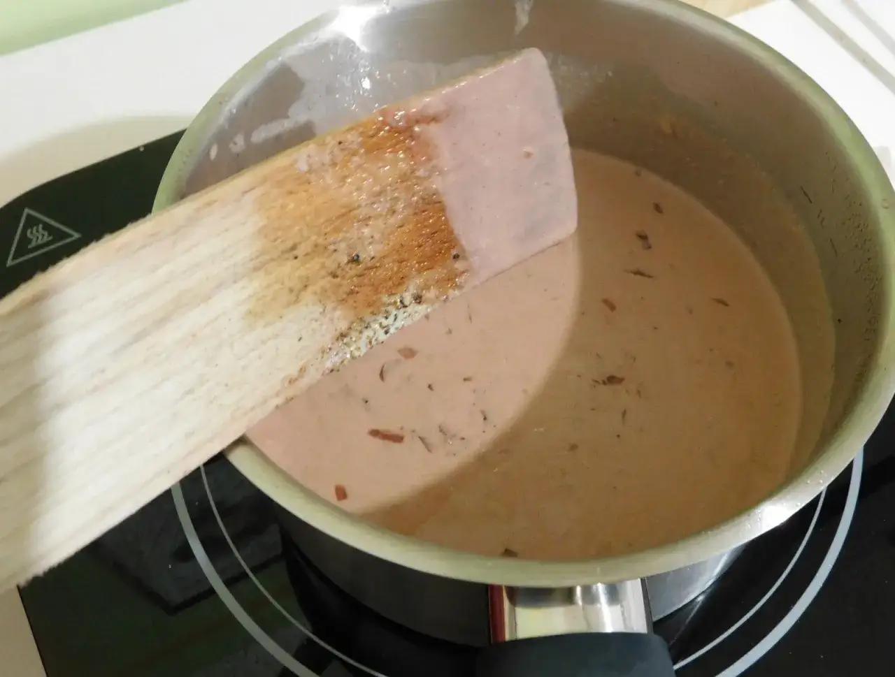 Une spatule en bois remue une sauce onctueuse dans une casserole. C'est le début d'une sauce porto facile et délicieuse.