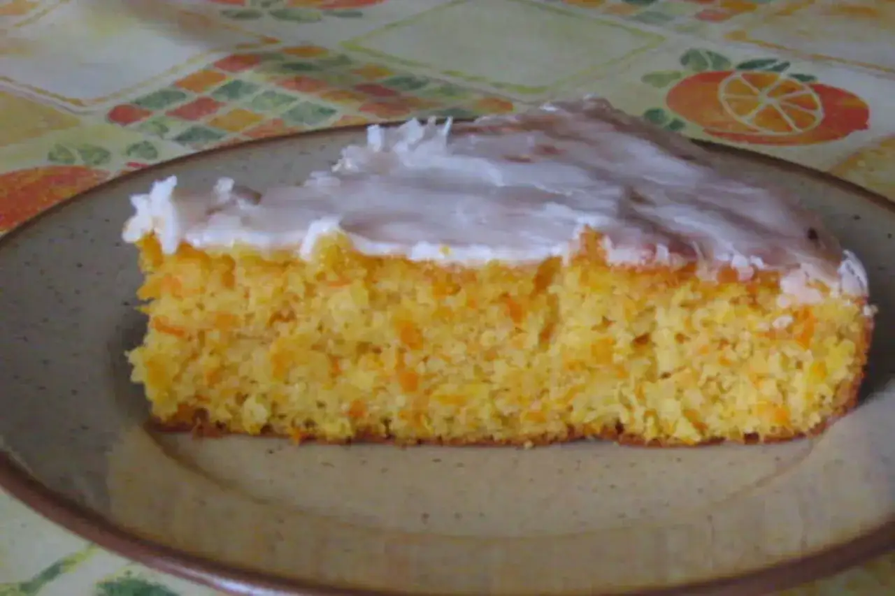 Tranche de gâteau moelleux aux carottes râpées, nappée d'un glaçage blanc crémeux. Un délice fait maison.