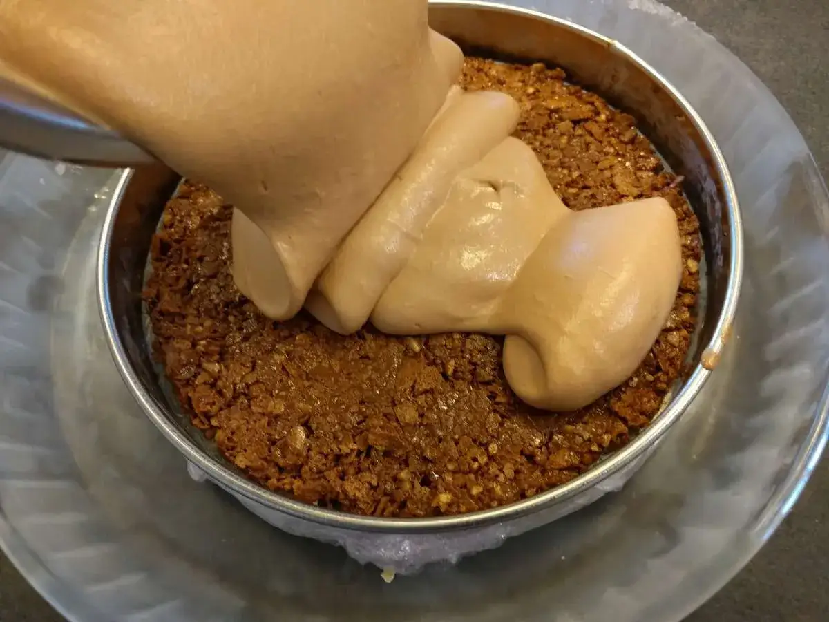 Garniture crémeuse versée sur une base croustillante dans un moule à gâteau.