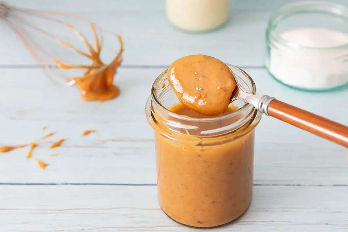 Une cuillère de confiture de lait onctueuse est prélevée d'un pot en verre. Un fouet dégouline de cette gourmandise.