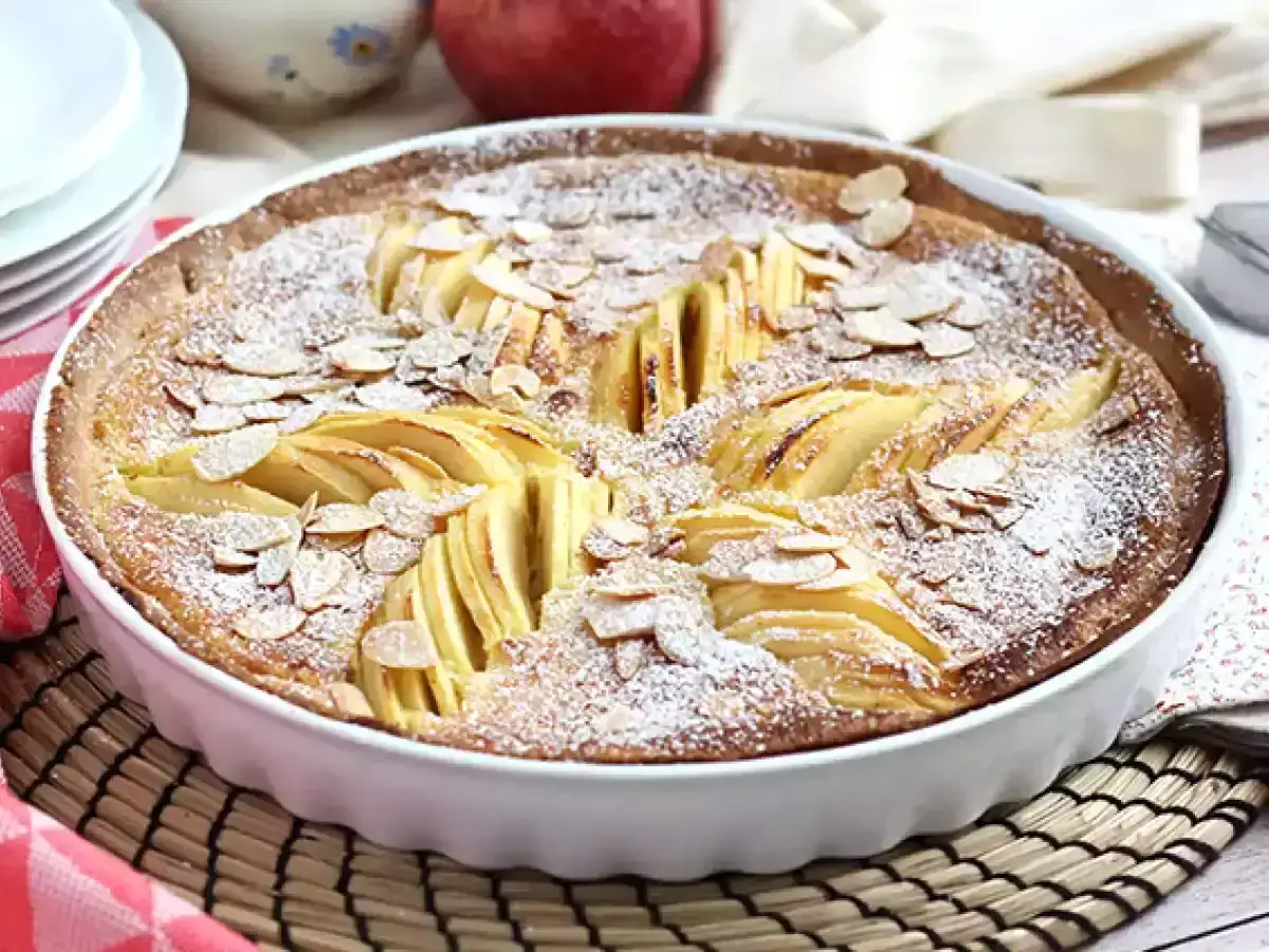 Tarte normande aux pommes, saupoudrée de sucre glace et d'amandes effilées, prête à être dégustée.