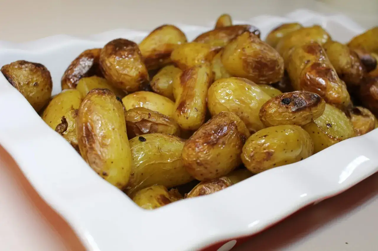 Un plat blanc rempli de pommes de terre nouvelles r&ocirc;ties, dor&eacute;es et app&eacute;tissantes.