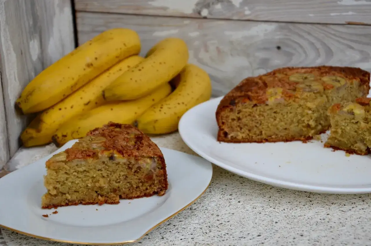 Tranches de délicieux gâteau yaourt banane, avec des bananes fraîches en arrière-plan.