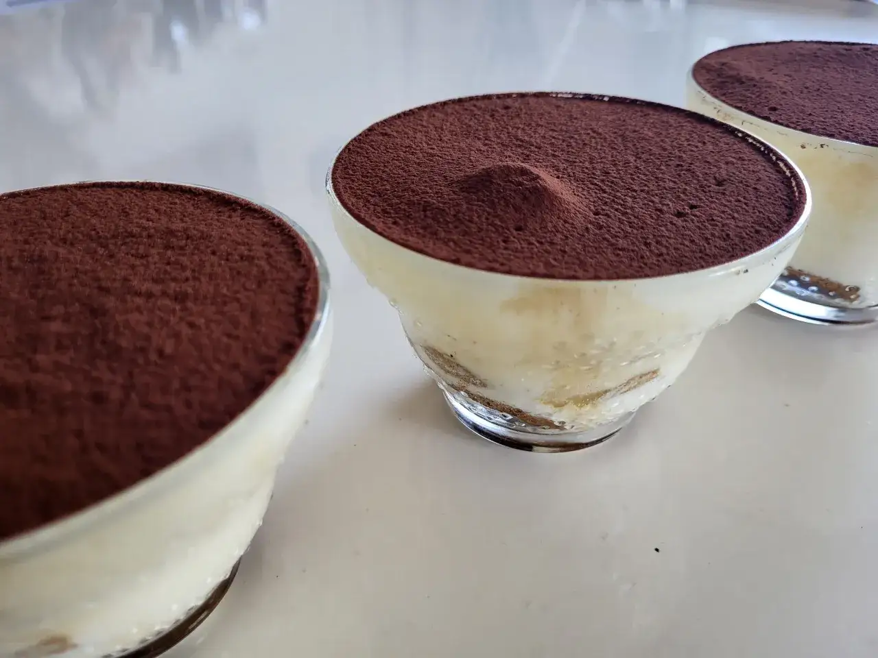 Trois verrines de tiramisu, prêtes à être dégustées. Une recette simple et délicieuse pour un dessert parfait.