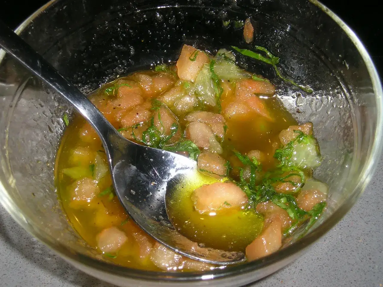 Cuillère dans un bol de sauce vierge aux tomates et herbes fraîches.