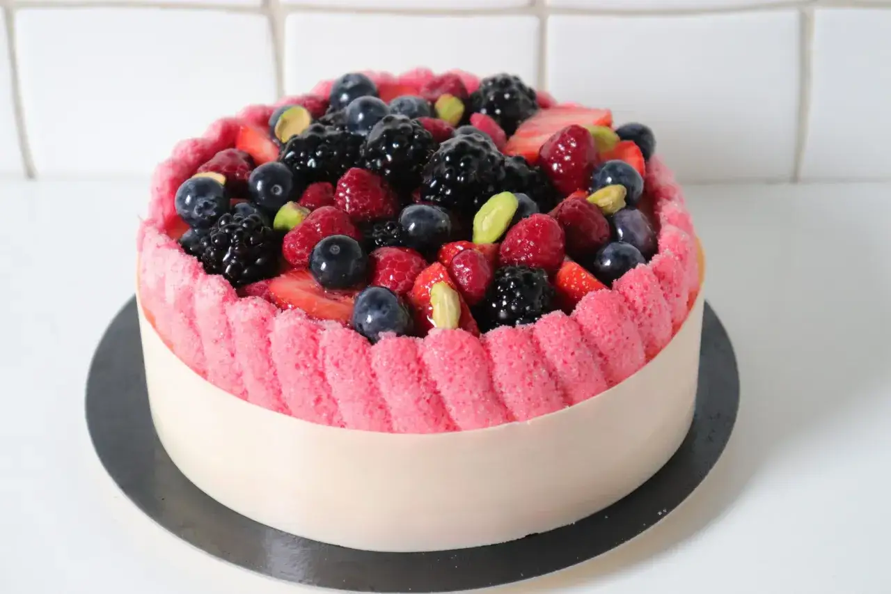 Charlotte aux fruits, un délice rose et blanc garni de baies fraîches et de pistaches.