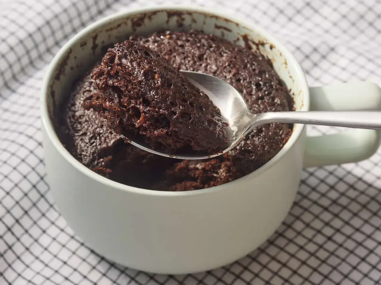 Une cuillère prélève un morceau moelleux d'un mug cake au chocolat, parfait pour une recette rapide et gourmande.