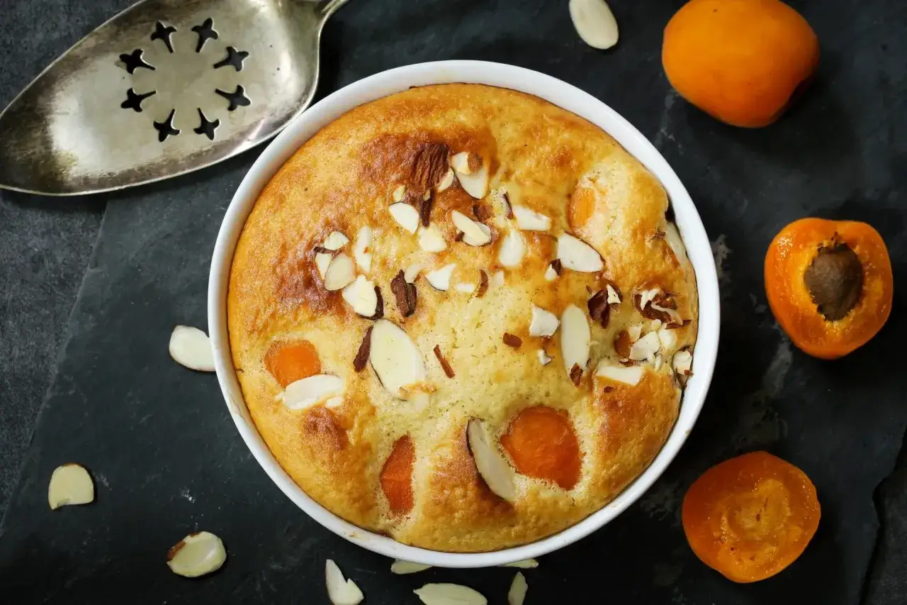 Clafoutis abricot doré, parsemé d'amandes effilées, prêt à être dégusté.
