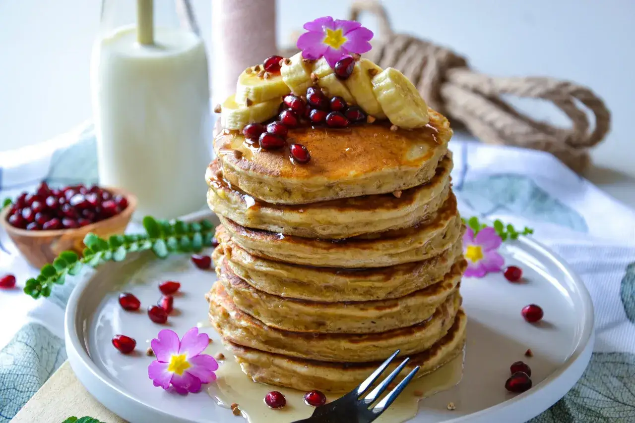 Pile de pancakes banane, garnie de fruits rouges, de rondelles de banane et de fleurs roses. Un délice pour le petit-déjeuner.
