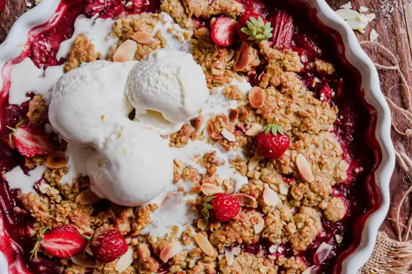 Un délicieux crumble rhubarbe fraise, garni de boules de glace à la vanille fondante et d'amandes effilées.