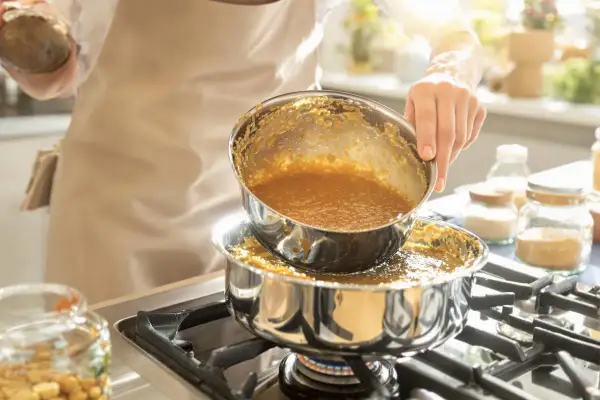 Une personne verse un liquide doré, du caramel à sec, d'une casserole à une autre sur une cuisinière.