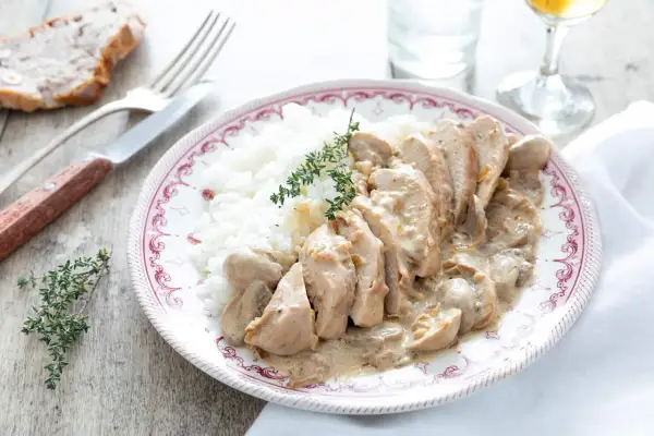 Une assiette de riz blanc avec des tranches de poulet nappées d'une sauce onctueuse au poulet crème champignon, garnie de thym frais.