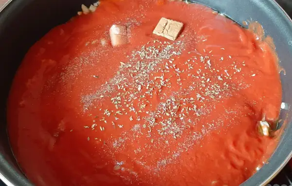 Sauce tomate maison mijote dans une poêle, agrémentée d'herbes et d'un cube de bouillon.