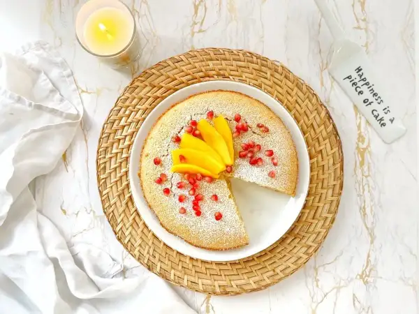 Un délicieux flan coco saupoudré de sucre glace, garni de mangue et de grenades. Une part manque, invitant à la gourmandise.