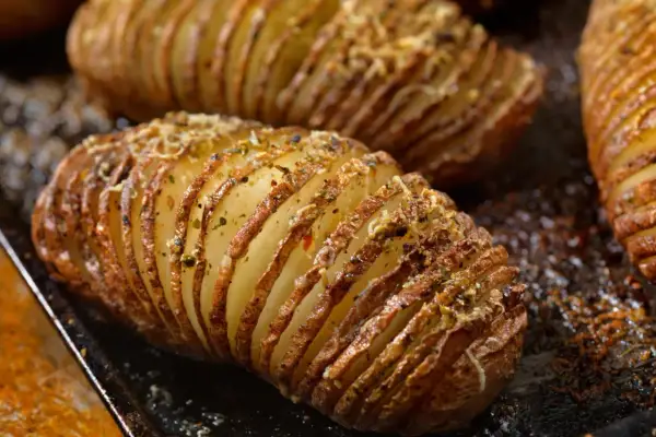Pommes de terre nouvelles coupées en accordéon, dorées et garnies d'herbes et de fromage, prêtes à être dégustées.