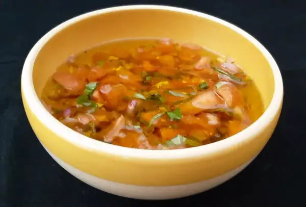 Un bol jaune contient une sauce vierge fraîche, avec des dés de tomates, des herbes vertes et une vinaigrette translucide.
