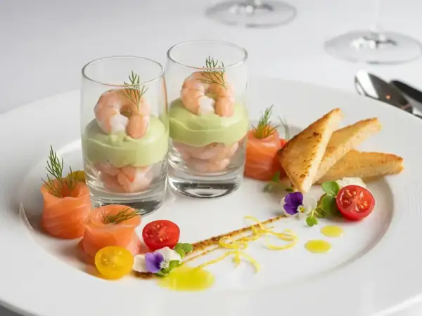Une délicieuse entrée froide : crevettes et avocat en verrine, saumon roulé, toasts grillés, tomates cerises et fleurs comestibles.