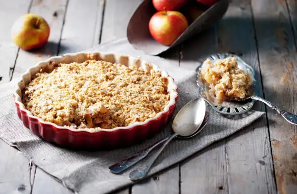 Un délicieux crumble pomme tout juste sorti du four, servi dans un plat rouge, avec une portion sur une cuillère ornée.