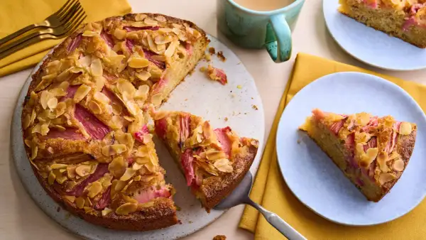 Un délicieux dessert rhubarbe gastronomique, un gâteau aux amandes effilées et à la rhubarbe rose, servi sur une assiette bleue.