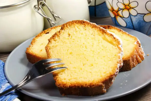 Tranches de gâteau au yaourt moelleux, saupoudrées de sucre glace, sur une assiette grise avec une fourchette.