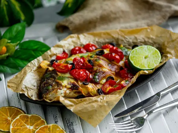 Dorade en papillote, savoureuse et colorée, garnie de tomates cerises, d'olives et d'une tranche de citron vert.