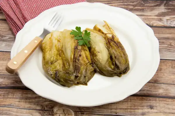 Deux endives fondue à la poêle, garnies de persil, sur une assiette blanche avec une fourchette.