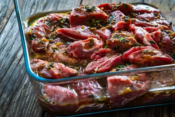 Morceaux de joue de porc marinés dans un plat en verre, prêts pour une délicieuse recette.