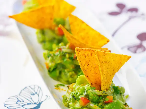 Guacamole maison, une recette facile et savoureuse. Des chips tortilla plongent dans ce délice vert.