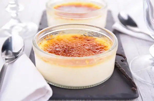 Deux délicieux crèmes brûlées, leur croûte caramélisée craquante, prêts à être dégustés avec une cuillère et une gousse de vanille.
