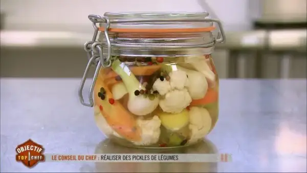 Un bocal de pickles de légumes colorés, comme ceux préparés par un Top Chef, rempli de chou-fleur, carottes et oignons.