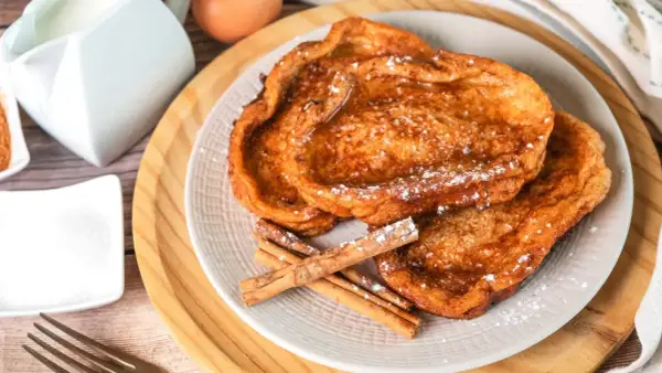 Trois tranches de pain perdu dorées, saupoudrées de sucre glace et garnies de bâtons de cannelle. Un délice pour le petit-déjeuner.