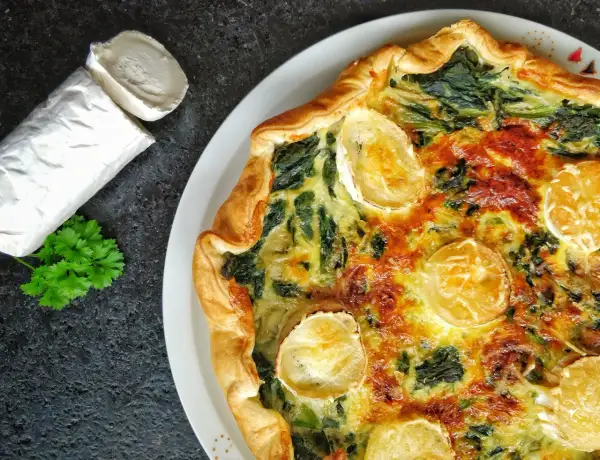 Tarte épinard chèvre dorée, avec du fromage de chèvre frais à côté et une touche de persil.
