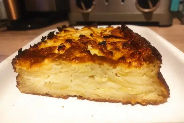 Tranche épaisse d'un délicieux cake aux pommes, avec une croûte dorée et caramélisée.