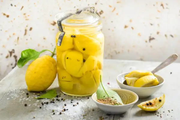 Un bocal de citrons confits au sel, prêts pour une recette citron confit sucre. Des épices et du gros sel parsèment la table.