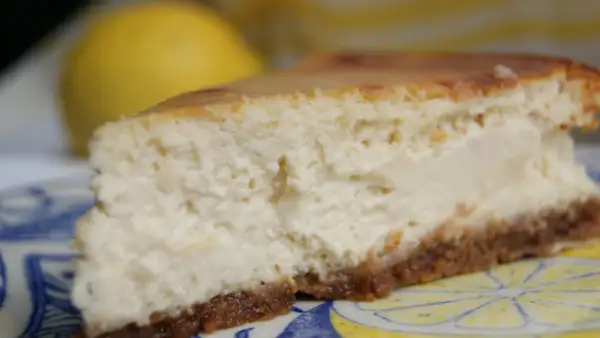 Tranche de cheesecake ricotta citron, crémeuse et légère, sur une assiette décorée de citrons.