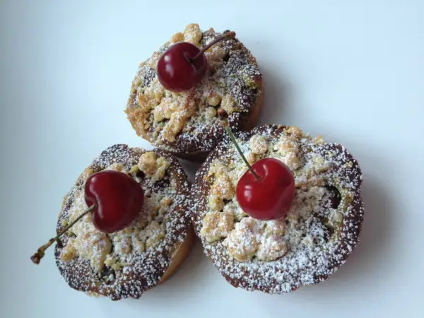 Trois petites tartelettes aux cerises, saupoudrées de sucre glace et ornées d'une cerise fraîche sur le dessus.
