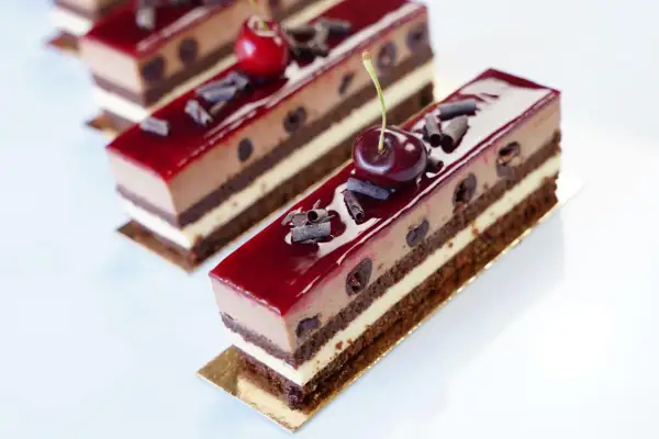 Délicieux entremets Forêt Noire, une symphonie chocolatée et cerise, parsemée de copeaux de chocolat et surmontée d'une cerise fraîche.