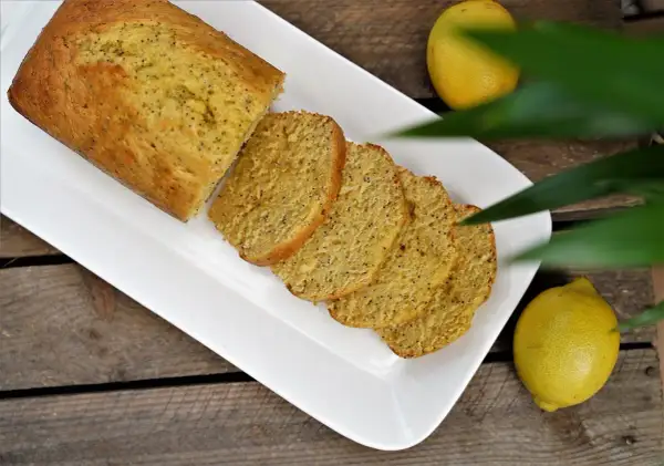 Un délicieux cake citron pavot, coupé en tranches, servi sur une assiette blanche, avec des citrons frais à côté.