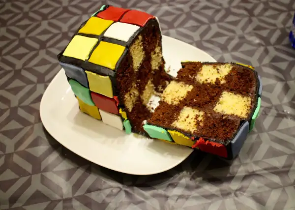 Un gâteau Rubik's cube, coupé en deux, révèle un intérieur marbré chocolat et vanille. Les couleurs vives du glaçage rappellent le célèbre casse-tête.