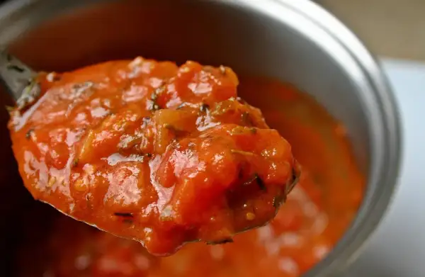 Une cuillère débordante de tomate concassée, parfumée d'herbes, prête à garnir un plat.