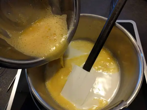 Préparation d'une recette crémeux vanille Michalak : on verse un mélange d'œufs battus dans une casserole contenant du lait et une spatule.