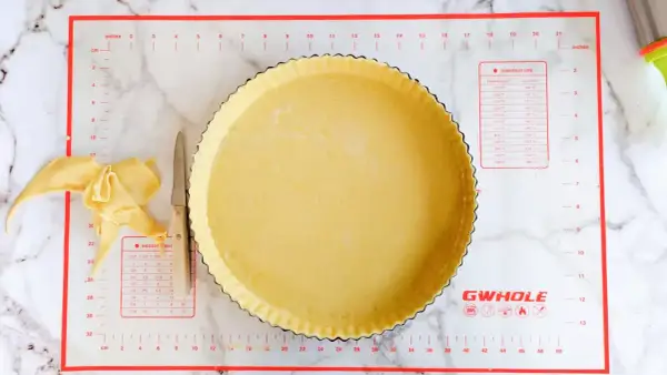 Pâte brisée salée prête à être garnie dans un moule à tarte. Des chutes de pâte et un couteau sont à côté.
