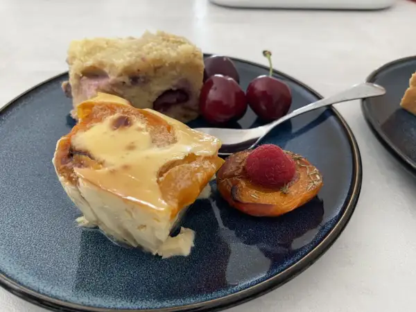 Un délice de clafoutis abricot, servi avec des cerises et une framboise sur une pêche rôtie.