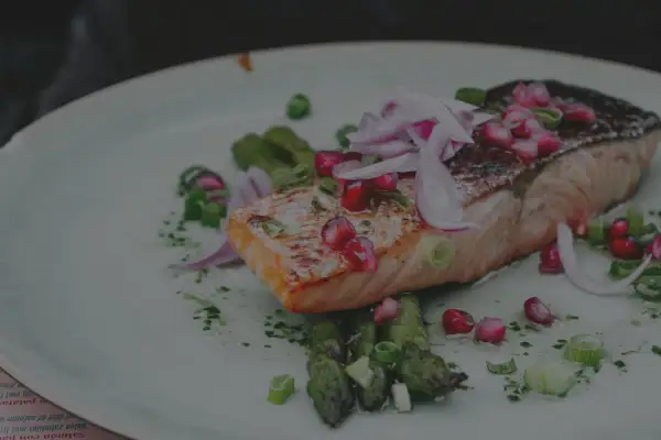 Un délicieux saumon air fryer, garni de grenade et d'oignon rouge, servi avec des asperges vertes.