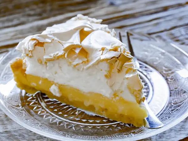 Une part de tarte au citron meringuée, avec sa crème jaune acidulée et sa meringue dorée, prête à être dégustée.