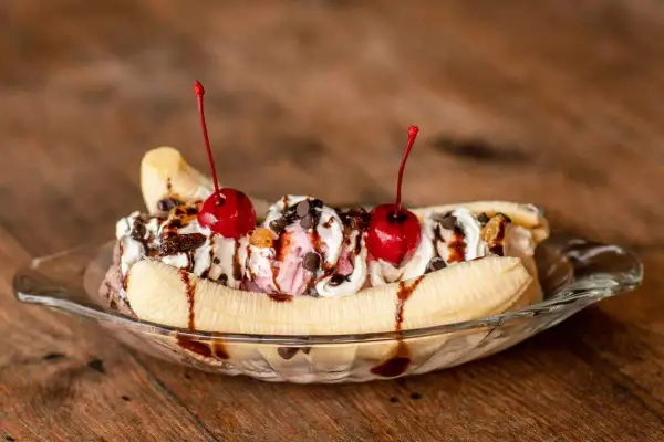 Un déliceux banana split garni de crème fouettée, de cerises et de sauce au chocolat, prêt à être dégusté.
