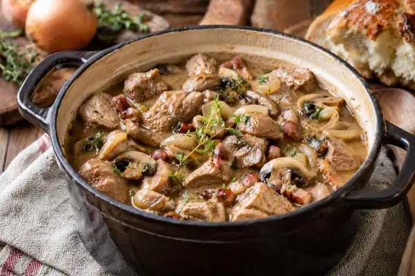 Un savoureux sauté de veau mijote dans une cocotte en fonte, garni de champignons, d'oignons et de lardons. Un plat réconfortant prêt à être dégusté.