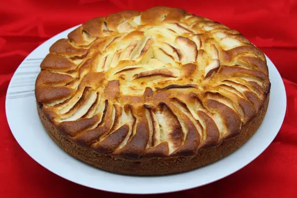 Un délicieux gâteau yaourt pomme, doré et appétissant, orné de fines lamelles de pommes disposées en rosace sur le dessus.