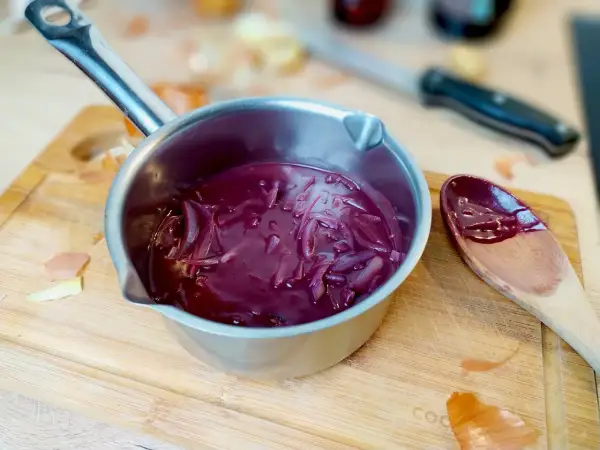 Sauce porto facile mijotant dans une casserole, avec des oignons rouges et une cuillère en bois.
