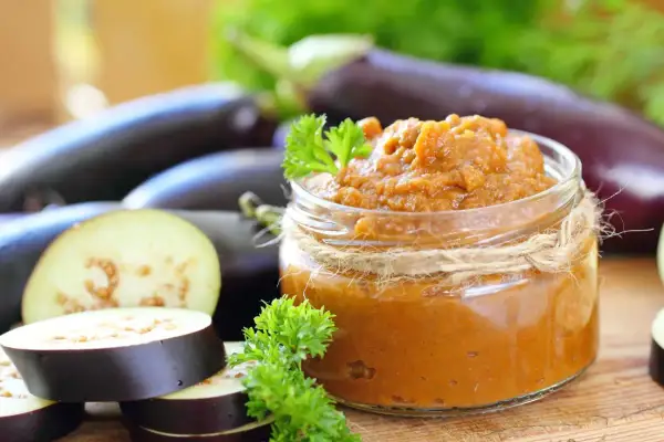 Un pot de caviar d'aubergine, garni de persil frais, entouré d'aubergines entières et tranchées.